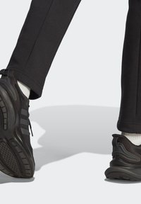 Svarta sportskor i strukturerat tyg, tre grå ränder och en gummisula. Kombineras med mörka byxor och vita strumpor.