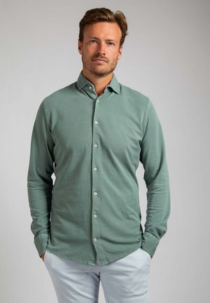 Langarm knoopbluso in een zachte groene stof met een gladde textuur, voorzien van een standaard kraag en witte knopen aan de voorkant.