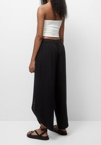 Pantalon noir à jambes larges avec une coupe décontractée et une taille élastique, associé à un crop top blanc texturé et des sandales noires à brides.