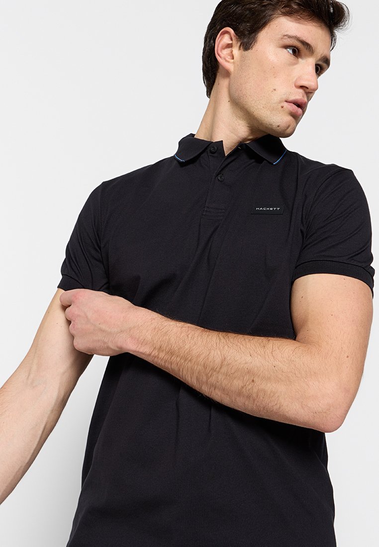 Camisa polo negra de manga corta, con un collar clásico y sutiles acentos azules. Elaborada en una tela suave, presenta un logo en el pecho.