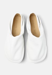 Scarpe slip-on in pelle bianca e morbida, con un design piegato, punta arrotondata e superficie liscia. Presentano una fodera interna di un leggero color beige.