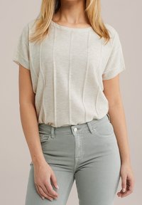 Haut tricoté beige clair à manches courtes avec côtes verticales, associé à un jean moulant vert clair, texture lisse, design décontracté.