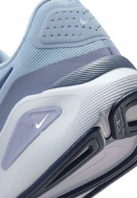 Primo piano del tallone di una scarpa da corsa Nike blu chiaro, con suola testurizzata, cuscino d'aria e piccoli loghi Nike swoosh bianchi.