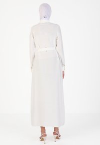 Long, white, fabric dress with long sleeves and a belted waist. Smooth texture, minimalistic design, paired with open-toed white heels.