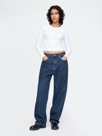 Hvit langermet crop-top med blå vidde denimbukser og svarte chunkboots. Stoffet ser glatt ut med en avslappet passform.