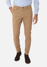 Chino beige con una vestibilità slim, realizzati in cotone, dotati di chiusura a bottone e tasche laterali. Indossati con stivali alla caviglia in suede neri.