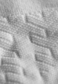 Texturiertes weißes Material mit einem weichen, plüschigen Erscheinungsbild, das erhabene geometrische Muster und feine Details auf der gesamten Oberfläche aufweist.
