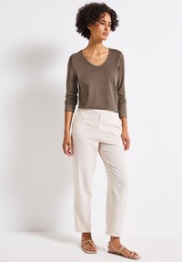 Olive green long-sleeve top with a V-neck, paired with cream-colored, tailored trousers and beige flat sandals. Smooth texture throughout.