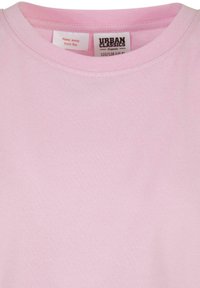 Rosa bomull t-skjorte med rund hals. Har et merke som sier "Holdes unna ild" og merkinformasjon. Glatt tekstur, enkelt design.