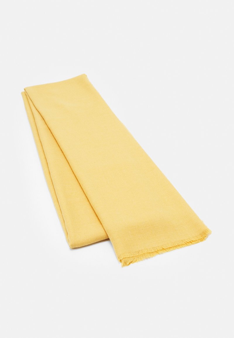 Tissu jaune doux plié soigneusement avec de courtes franges sur un bord, présenté sur un fond clair uni.