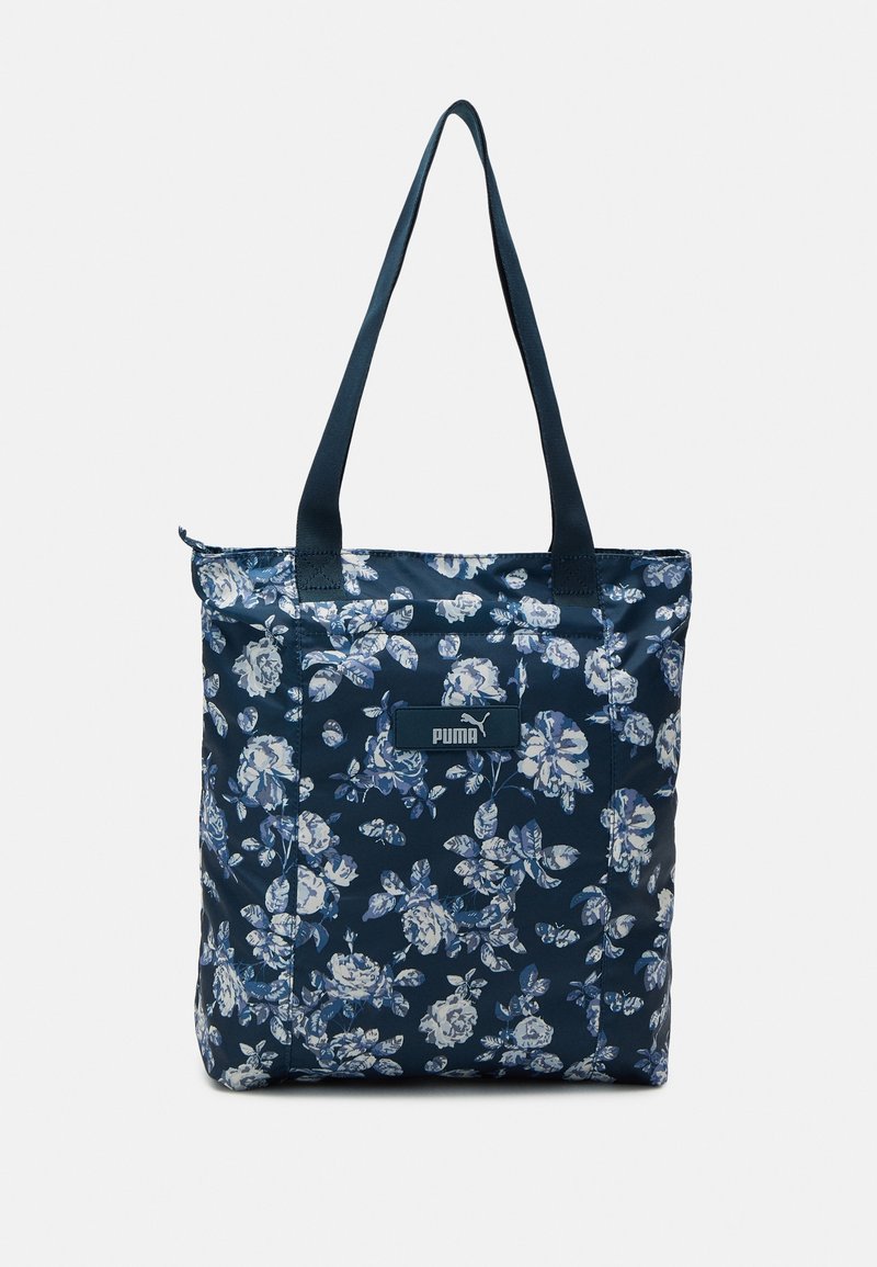 Marineblauw draagtas met een bloemenpatroon in lichtblauw. Gemaakt van glanzend materiaal, met schouderbanden en een logo-opdruk aan de voorkant.