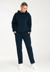 Granatowy sweatshirt z wysokim kołnierzem, zestawiony z pasującymi spodniami cargo z przednimi kieszeniami i elastycznymi mankietami, noszony z białymi sneakersami.