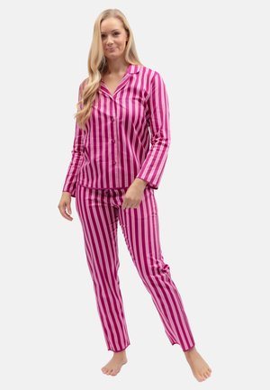 Frau steht barfuß und trägt ein rosa-weiß gestreiftes Langarm-Pyjama-Oberteil mit Knöpfen und passende Hose.