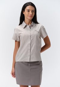 Blusa grigia chiara a maniche corte con un motivo a foglie, chiusura bottoni sul davanti e taschino sul petto, abbinata a una gonna grigia coordinata.