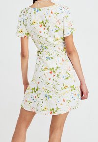 Vestido blanco de manga corta con un patrón floral en verde, rojo y azul. Tiene una cintura ajustada y una falda fluida.