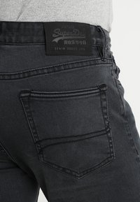 Vaqueros de mezclilla negra con un diseño vintage, que cuentan con una cintura texturizada, etiqueta de cuero y costuras sutiles en los bolsillos traseros.