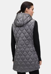 Szary pikowany kamizelka z kapturem, z diamentowym wzorem i gładką fakturą, noszona na czarnej bluzce z długim rękawem.