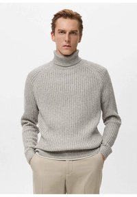 Grijze geribbelde coltrui van gebreide stof, met lange mouwen en een aansluitende pasvorm, gecombineerd met beige broek.