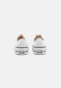 Fehér vászon sportcipők alacsony fazonnal, fekete gumitalppal, fekete-fehér csíkozással és "Converse All Star" logóval a saroknál.