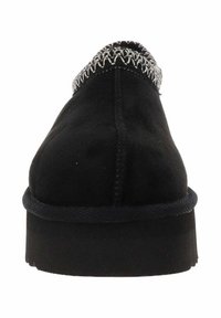 Zapatilla de ante negra con costuras texturizadas en el cuello, suela plana y diseño de punta redonda. Acentuada con un borde oscuro.