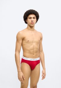 Κόκκινο βαμβακερό εσώρουχο με λευκή ελαστική μέση που φέρει το λογότυπο "TOMMY HILFIGER". Σχεδιασμένο για άνεση, με εφαρμοστή γραμμή και χαμηλή μέση.