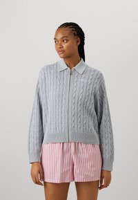 Light grey zip-up cardigan with cable knit design and ribbed hem, paired with pink and white striped shorts.