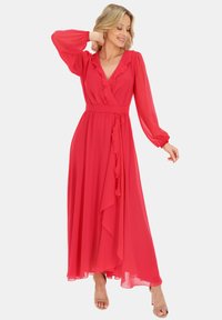 Czerwona zwiewna sukienka z chiffonu z długimi rękawami, falbanami przy dekolcie i u dołu oraz przewiązanym w pasie paskiem, tworząca zwiewną sylwetkę.
