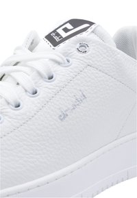 Sneaker in pelle bianca con superficie testurizzata, lacci bianchi, suola in gomma e branding grigio sul lato e sulla linguetta. Dettagli di cucitura sottili.