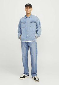 Lichtblauwe spijkerjacket met twee borstzakken, gecombineerd met bijpassende jeans en zwarte sneakers. Zwarte pet met een logo.