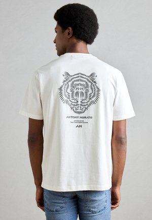 Cream cotton t-shirt featuring a black tiger graphic on the back, with brand name "ANTONY MORATO" and establishment year printed below.
