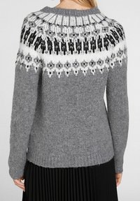 Pull gris en tricot avec un empiècement à motif noir et blanc. Caractéristiques manches longues et ourlet côtelé. Texture douce et coupe ample.