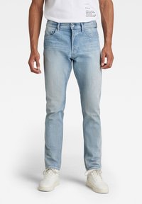 Ljusblå denimjeans med slim fit, med en standard femfickdesign och kontrasterande sömmar. Bärs med vita sneakers.