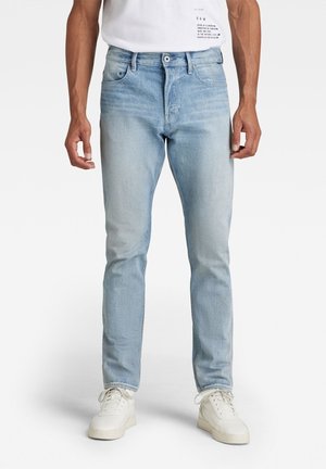 Vaqueros de mezclilla azul claro con un corte ajustado, que cuentan con un diseño estándar de cinco bolsillos y costuras en contraste. Llevados con zapatillas blancas.