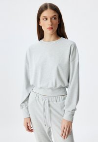 Helles graues, geripptes Sweatshirt mit Rundhalsausschnitt und langen Ärmeln. Mit elastischem Bund und lockerer Passform. Weicher Stoff.