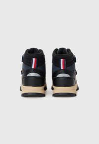 Μαύρα μποτάκια τύπου high-top με μαλακό κολάρο, συνθετικό πάνω μέρος και μπεζ σόλα. Περιλαμβάνουν λεπτομέρεια κάθετης ρίγας σε κόκκινο, λευκό και μπλε χρώμα.