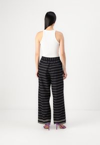 Μαύροι παντελόνια σε ευρύ κόψιμο με γεωμετρικό σχέδιο, ελαστική μέση και αντιθετικό σχέδιο. Συμπληρωμένα με μωβ ψηλοτάκουνες σαγιονάρες.