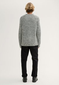 Suéter gris de punto con un acabado texturizado, cuello redondo y hombros caídos, combinado con pantalones negros y zapatos negros.