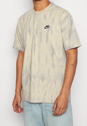 Lysebeige tie-dye T-shirt lavet af bomuld, med et lille sort Nike-logo på brystet og korte ærmer. Blød tekstur og afslappet pasform.