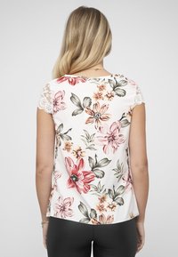 Bloemenblouse met een witte basis en bloemen in roze, oranje en groen, kanten mouwtjes en een losse pasvorm. Zachte textuur en lichtgewicht ontwerp.