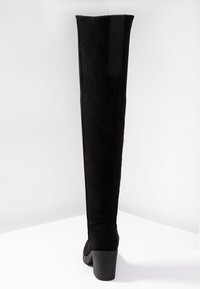 Botas negras de ante por encima de la rodilla, con un tacón robusto, caña texturizada y panel elástico para un mejor ajuste.