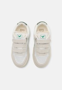 Valkoiset lenkkarit vaaleanbeigeistä mokasta valmistetuilla yksityiskohdilla, joissa on rei'itetty muotoilu ja kolme tarranauhaa. Vihreä logo kielekkeessä ja sivussa.