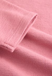 Gros plan sur un tissu rose en maille gaufrée plié, montrant la texture détaillée et les coutures sur un poignet de manche.