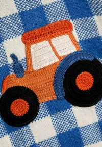 Gehäkelter orangefarbener Traktor mit schwarzen und blauen Rädern auf einem blau-weißen karierten Strickstoff-Hintergrund.
