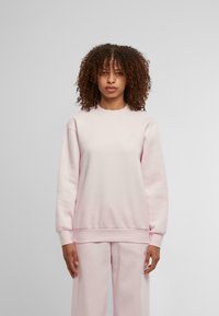 Világos rózsaszín kapucn nélküli pulóver, puha anyagból készült, kerek nyakkal és bordás mandzsettákkal. Egyszerű dizájn, látható minták vagy grafikák nélkül.