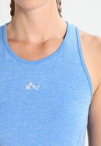 Jasnoniebieski sportowy top bez rękawów wykonany z teksturowanej tkaniny. Posiada okrągły dekolt i mały wzór logo w pobliżu środka.