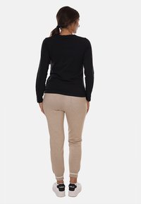 Maglietta nera a maniche lunghe e pantaloni jogger beige in morbido tessuto, con polsini elasticizzati e sneakers bianche con dettagli neri sul tallone.