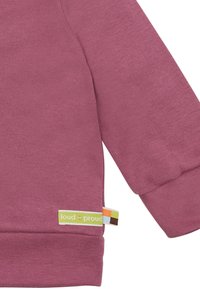 Felpa bordeaux con maniche lunghe, polsini a costina e un'etichetta verde e multicolore "loud + proud" sull'orlo. Texture morbida.