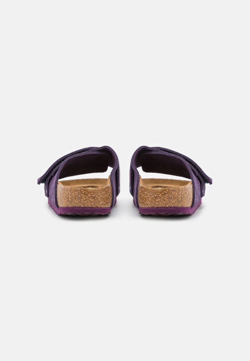 Lila Wildledersandaletten ohne Rücken mit einem Korkfußbett, strukturiertem Profil und einer leicht erhöhten Plattform. Einfaches Design ohne zusätzliche Akzente.