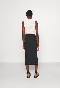 Top sans manches beige en tricot avec une finition texturée, associé à une jupe midi noire ajustée à côtes. Le modèle porte des bottes beiges à la cheville et des chaussettes noires.