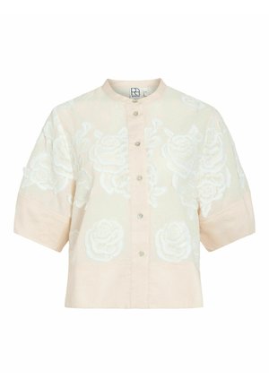 Chemise beige à manches courtes avec boutons, broderie florale blanche, col rond et coupe ample et carrée.